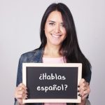 Young woman holding sign "Hablas español?""